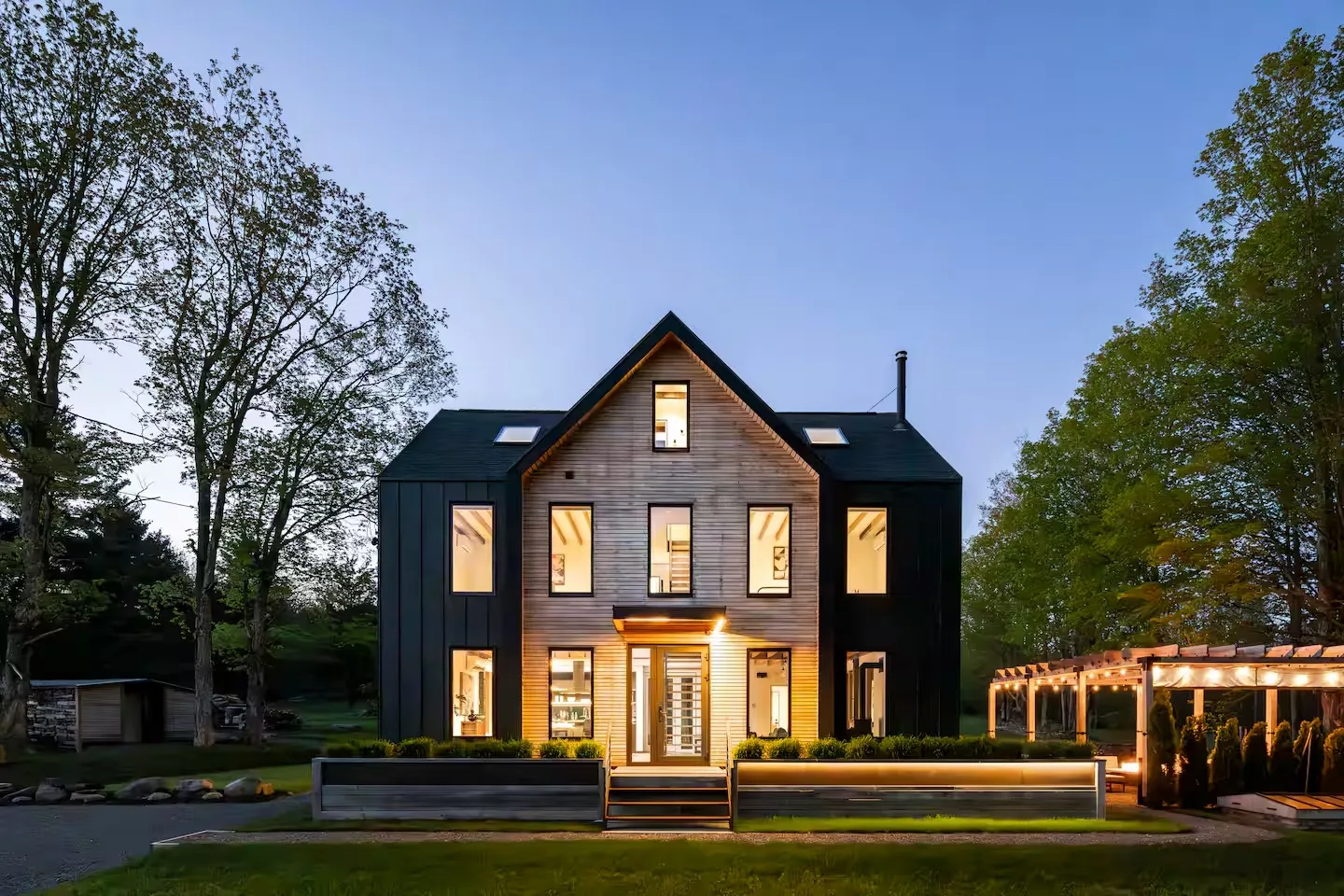 Modern farmhouse with black and wood siding lit up at dusk